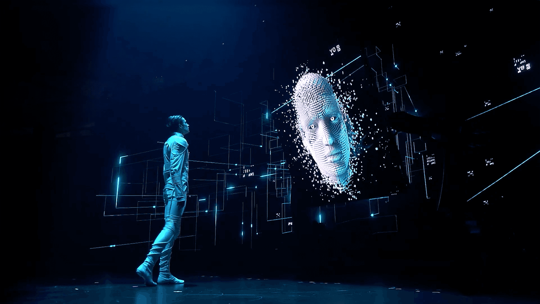 A performer looking at the face of an Artificial Intelligence on LED screens as part of a multimedia performance at the Global AI Summit 2022