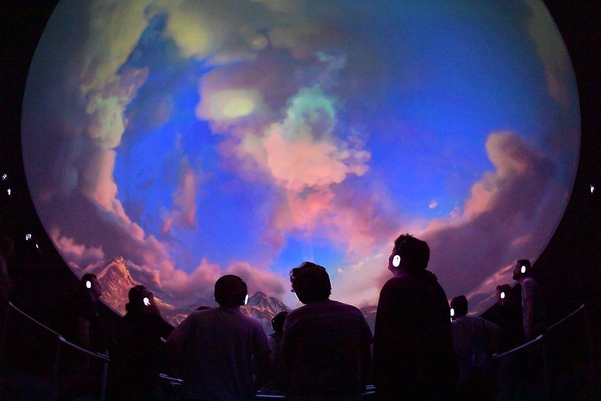 People looking at a projection inside the Immersive Ring Experience dome at the “Halo: Outpost Discovery” exhibition